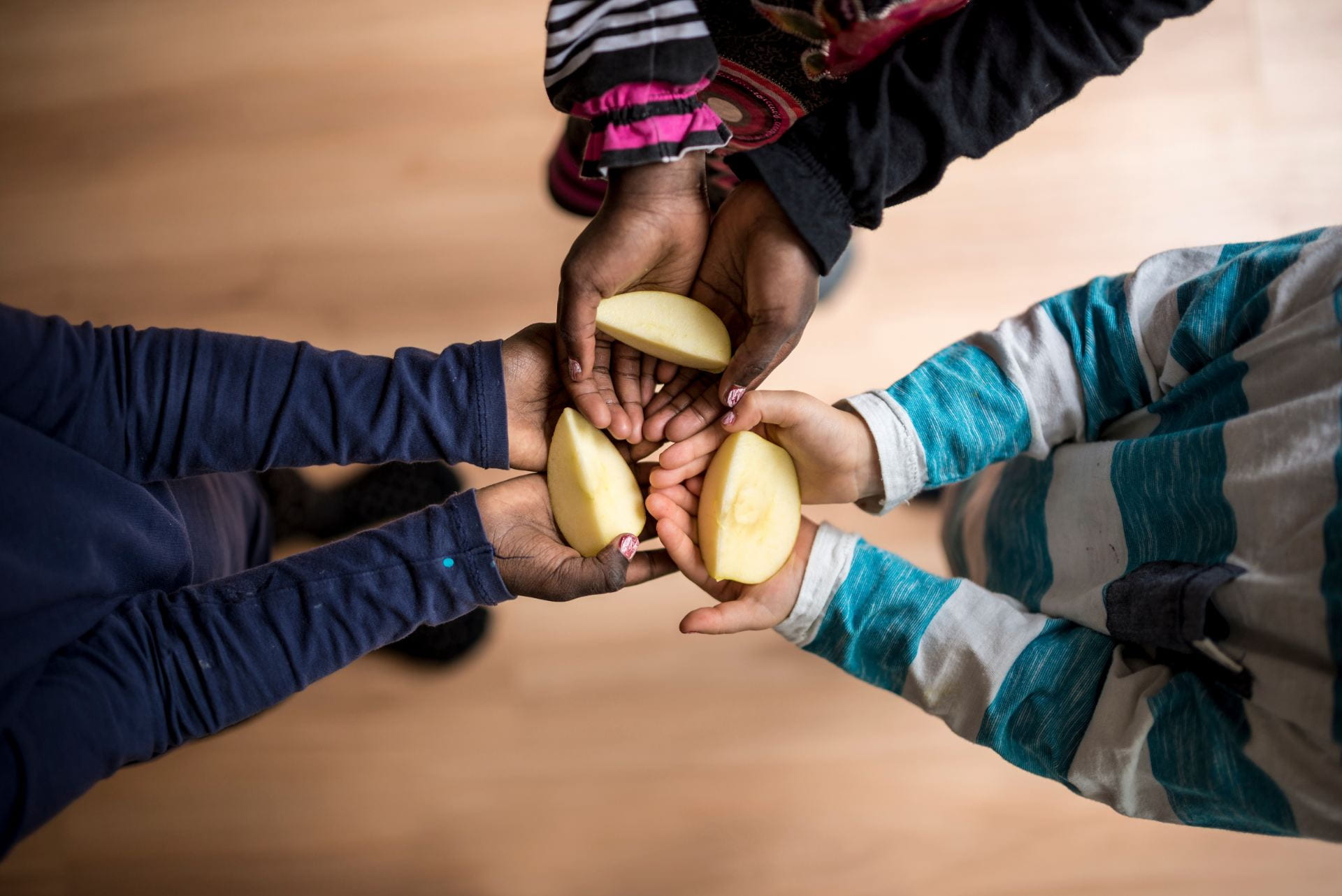 Top view of three kids each holding a piece of apple in the palms of their hands.